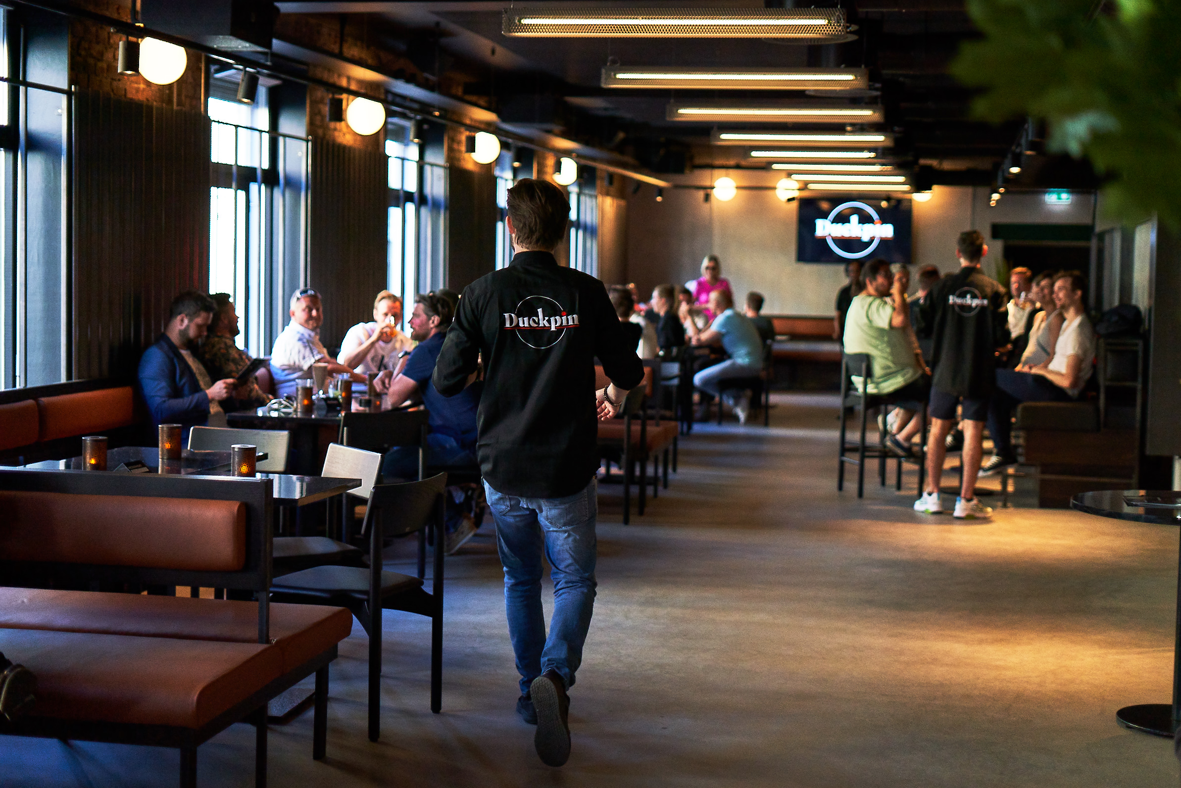 An employee wearing a Duckpin shirt makes his way through the warmly lit bar room.