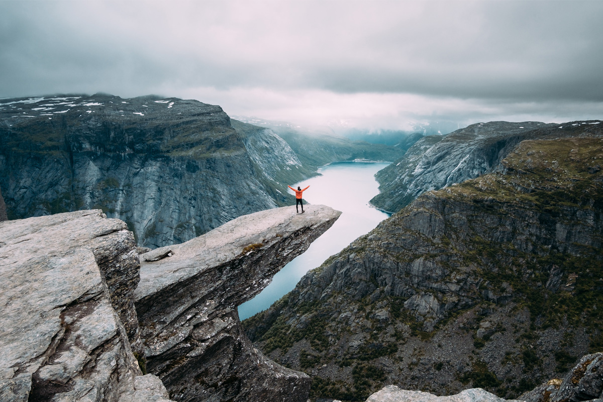 Person in orange jacket standing with arms in the air overlooking a spectacular view.